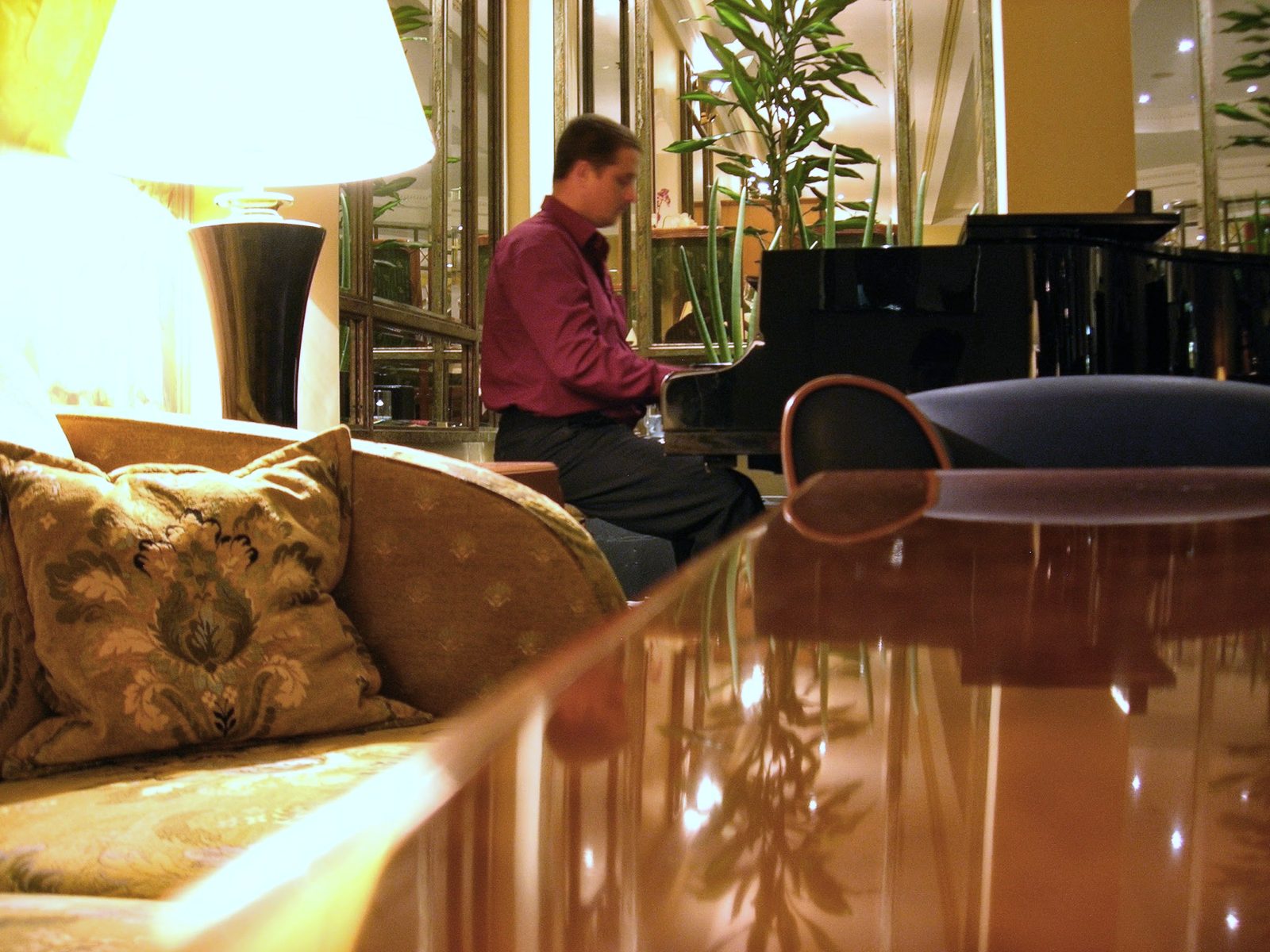 Salón de hotel con un piano de cola al fondo y un sofá con cojines dorados en primer plano