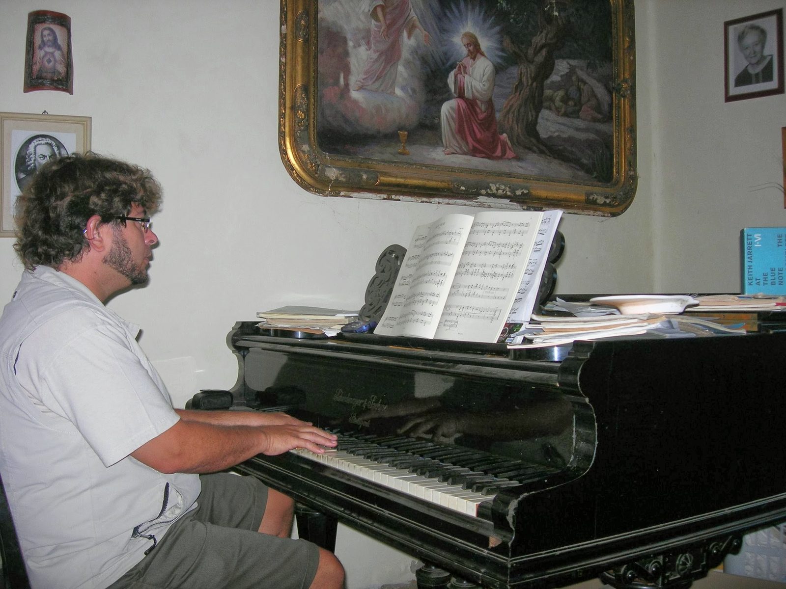 Yan Kayary trabajando con partituras en un piano de cola, con un cuadro al fondo