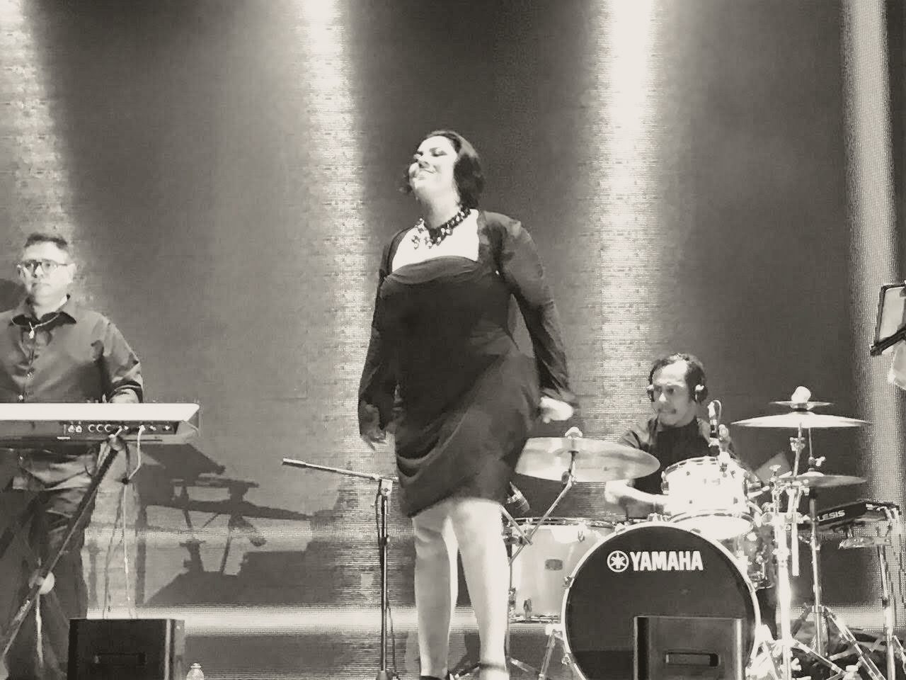 Yan al teclado en un escenario iluminado, con una cantante y batería