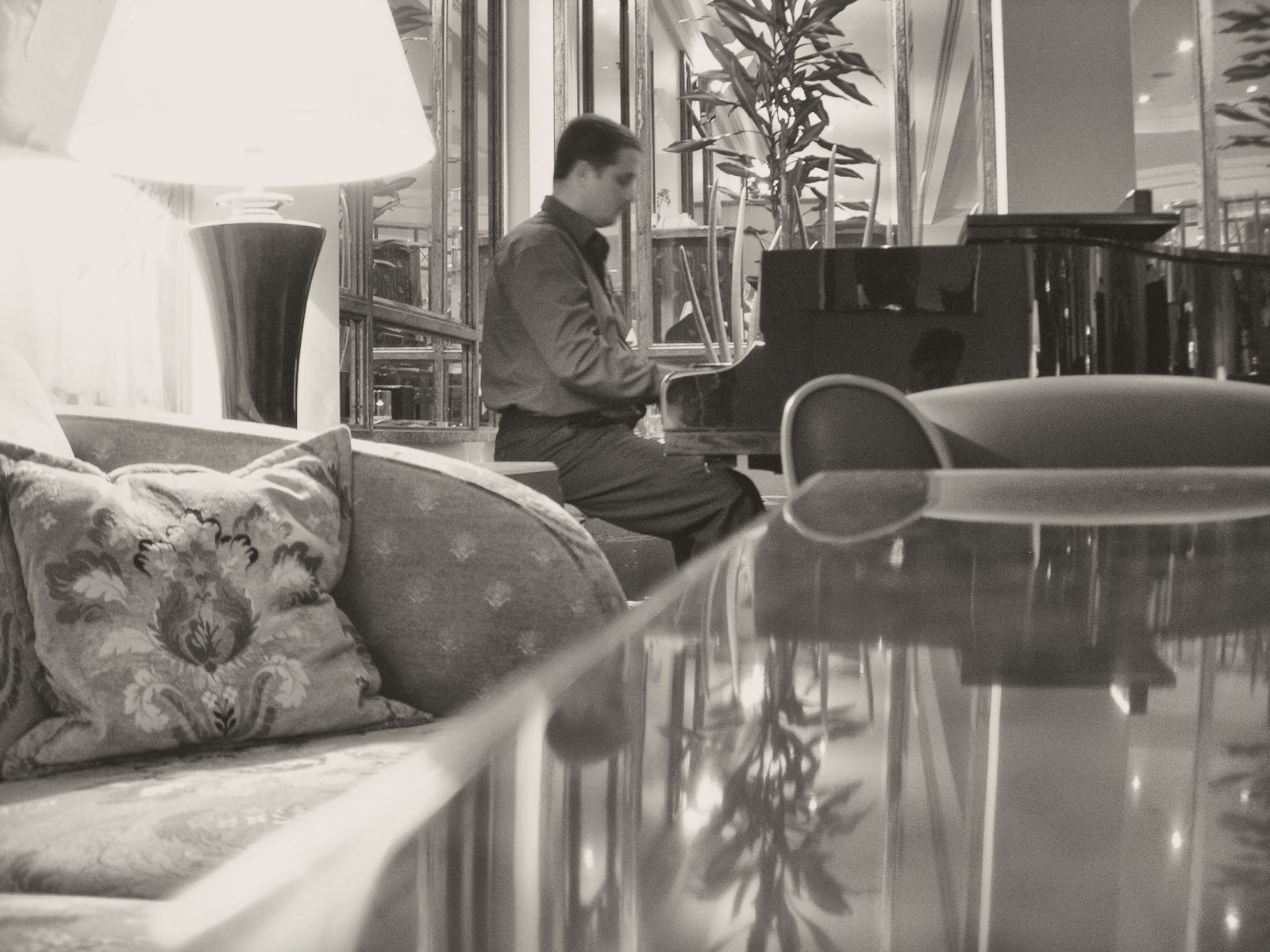 Salón de hotel con un piano de cola al fondo y un sofá con cojines dorados en primer plano