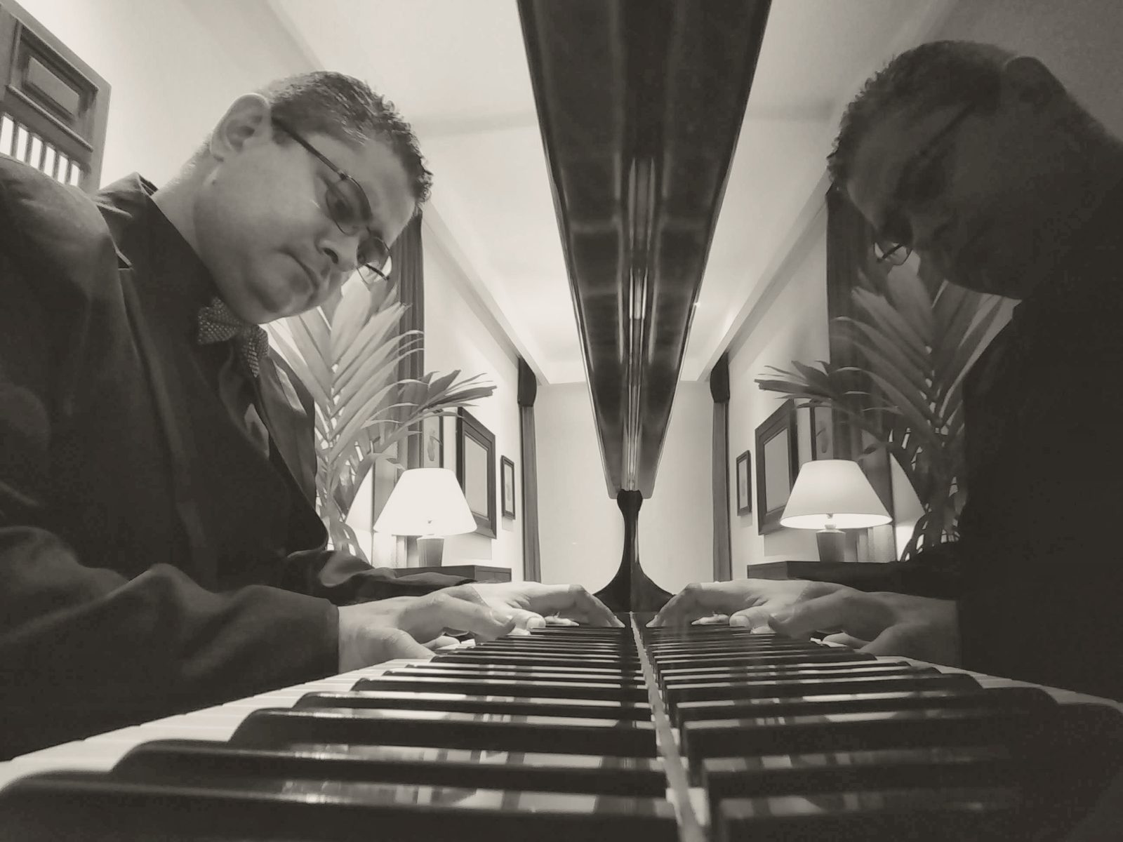 Manos sobre el teclado de un piano de cola, con el reflejo de la tapa